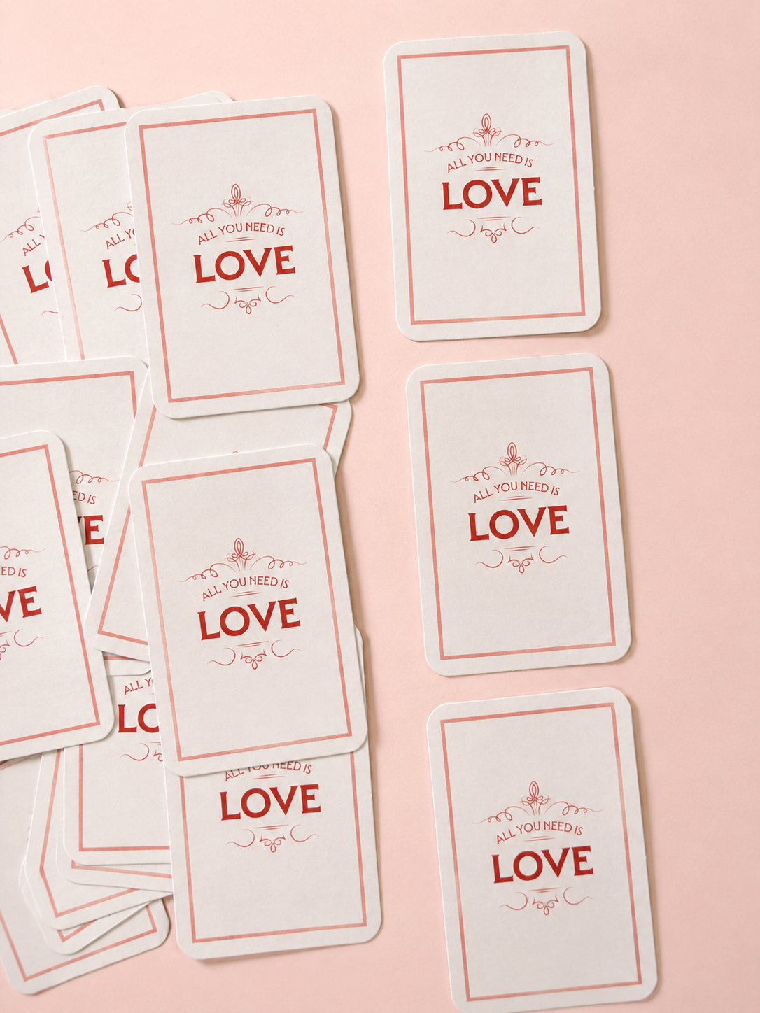 All You Need Is Love mini cards with red typography and decorative border, arranged on a soft powder-pink background.