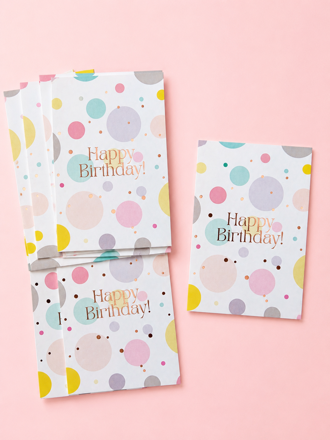 Pastel Happy Birthday greeting cards with colourful polka dots and rose gold lettering, arranged on a soft powder pink background.