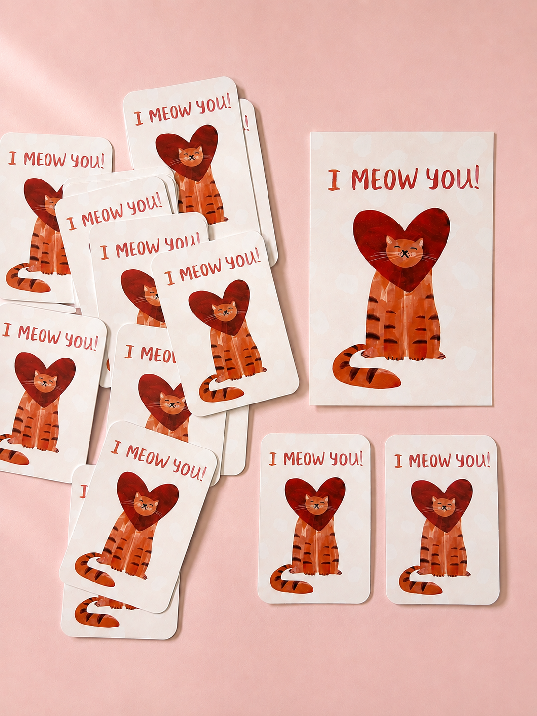 I Meow You illustrated greeting cards featuring an orange cat framed by a red heart, arranged on a soft powder pink background.