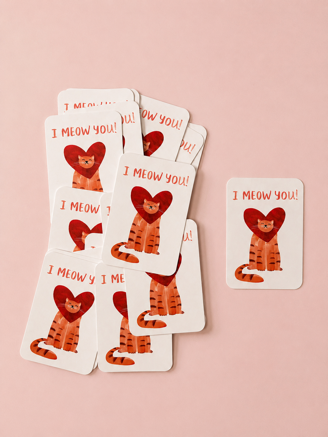 I Meow You greeting cards featuring an orange cat framed by a red heart, arranged on a soft powder pink background.