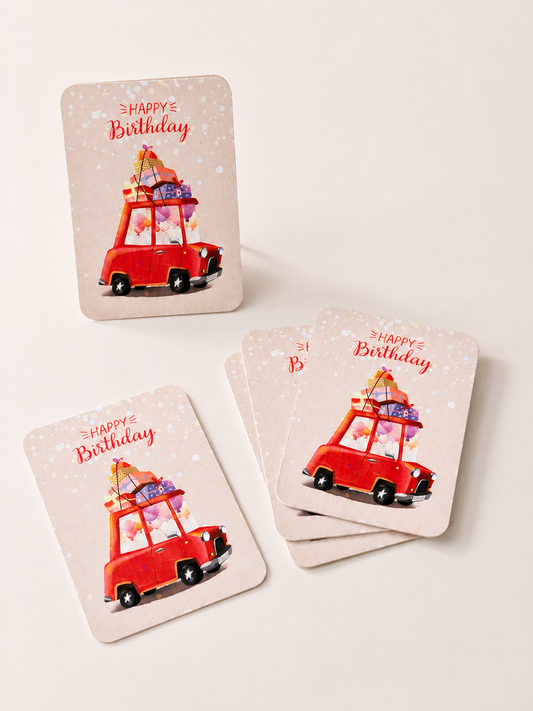 Happy Birthday cards arranged in small stacks on a bright pink background, featuring a red car loaded with colourful gifts