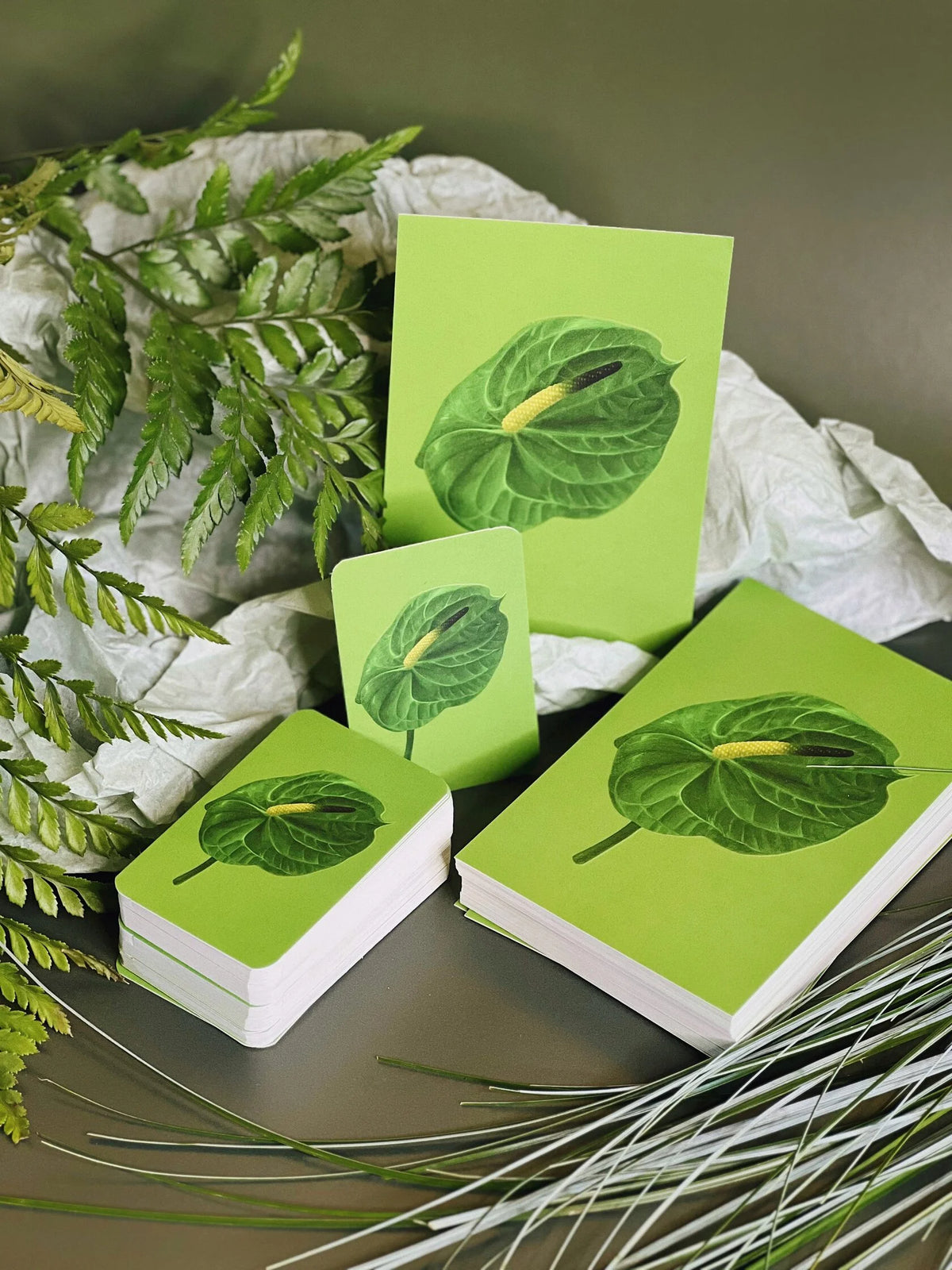 Green greeting cards and mini cards with an embossed anthurium leaf illustration, shown standing and in stacks, styled with ferns.