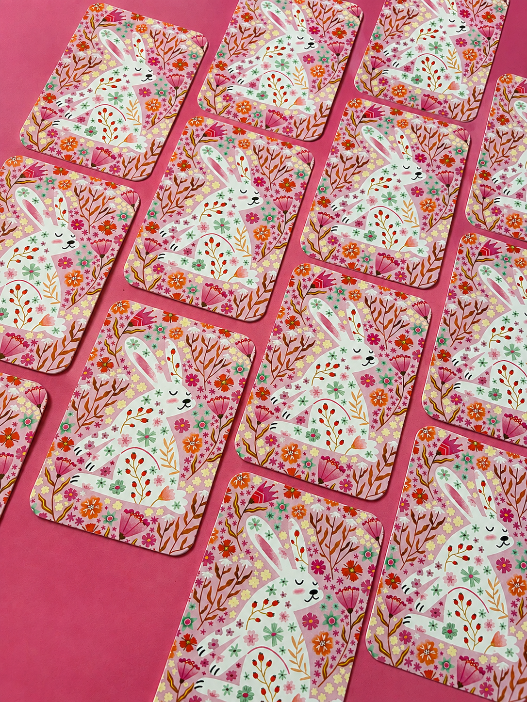 Pink floral bunny cards arranged in rows on a bright pink background, featuring a white rabbit surrounded by colourful flowers and botanical details
