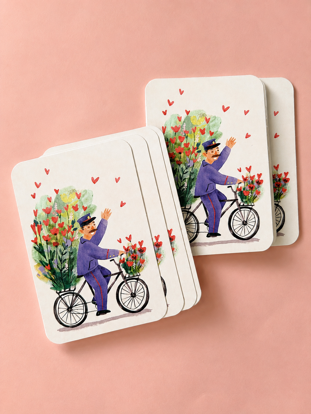 Illustrated mini cards featuring a flower-filled bicycle and a waving cyclist, arranged in two stacks on a soft powder-pink background