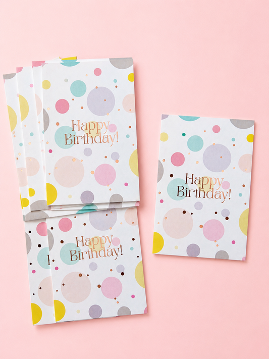 Pastel Happy Birthday greeting cards with colourful polka dots and rose gold lettering, arranged on a soft powder pink background.