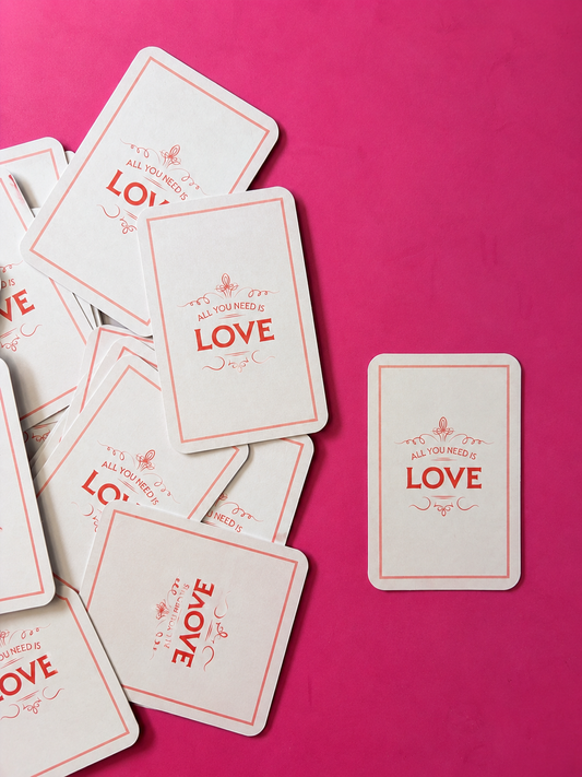 All You Need Is Love greeting cards with coral typography and decorative border, arranged on a bright magenta background.