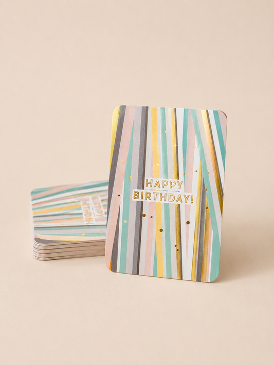 Pastel striped Happy Birthday card with gold foil details, displayed with a stack of matching cards on a warm neutral background.