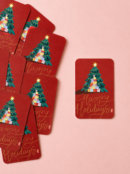 Red “Happy Holidays” mini cards featuring a decorated Christmas tree and colourful gifts, arranged on a soft powder pink background.