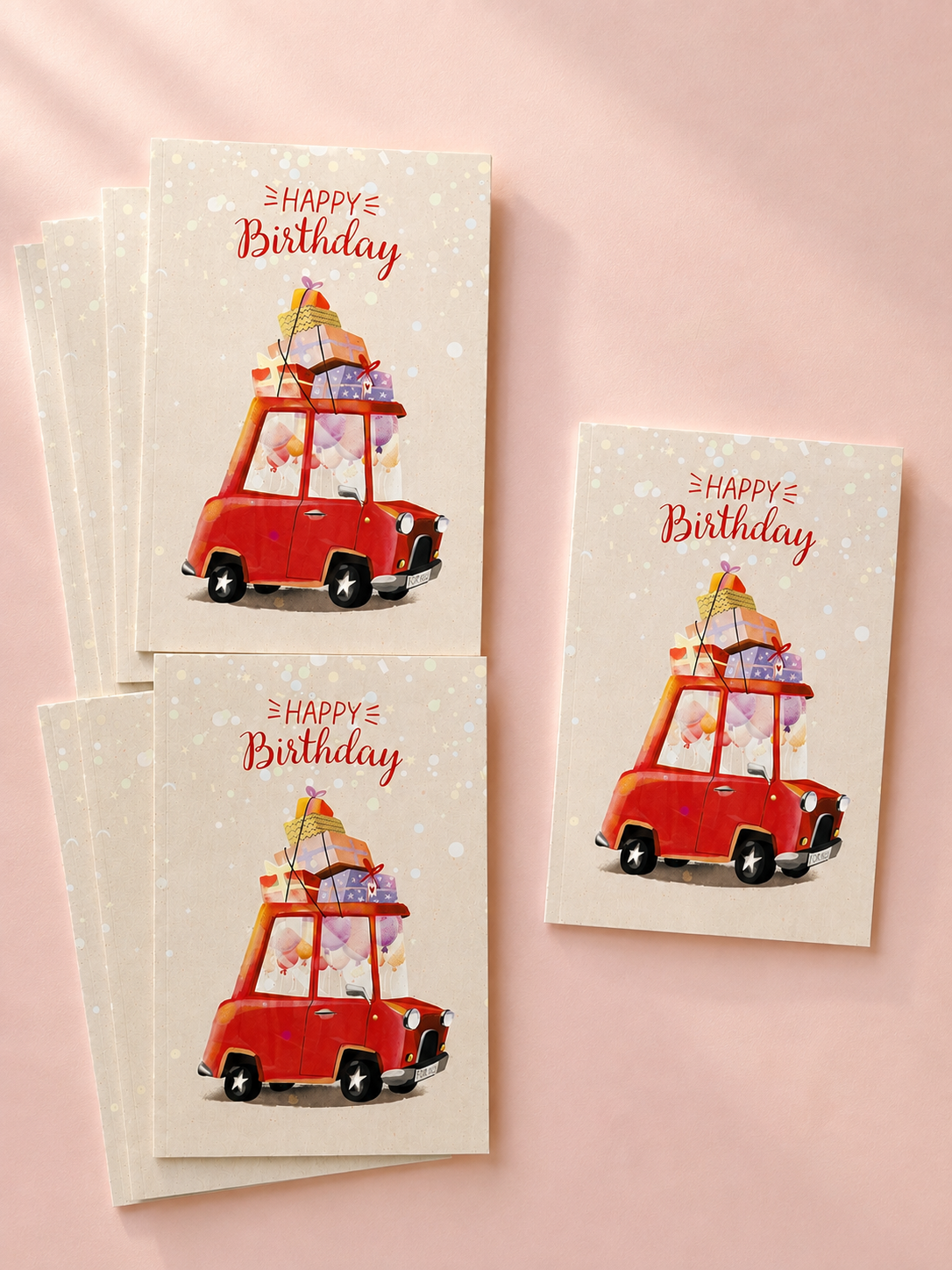 Birthday greeting cards featuring a red car filled with balloons and gifts, with “Happy Birthday” lettering on a soft pink background.