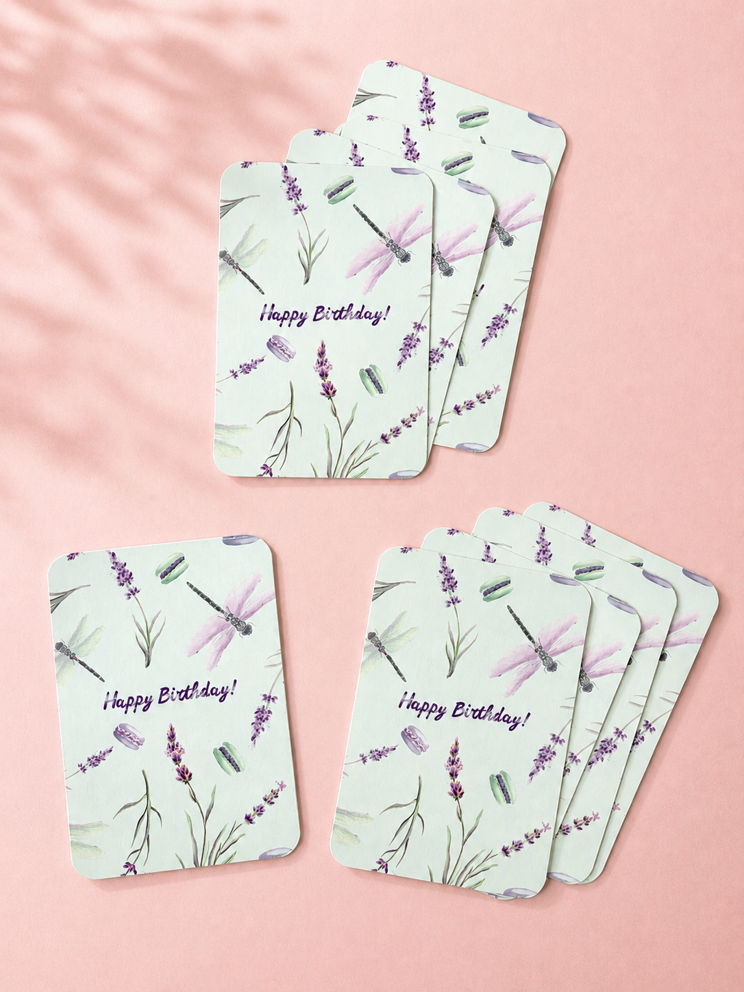 Mint green Happy Birthday cards with watercolor lavender, dragonflies and macarons, arranged on a soft powder pink background