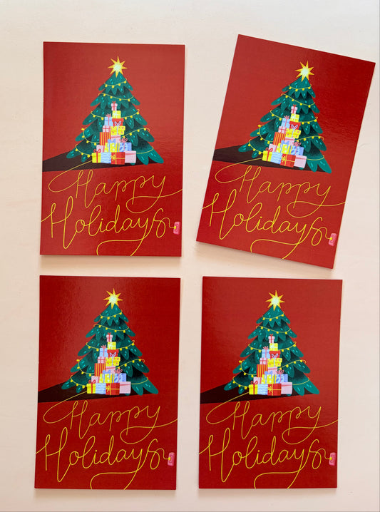 Four red Christmas greeting cards featuring a decorated Christmas tree, colourful presents and gold “Happy Holidays” lettering, arranged on a soft powder-pink background.
