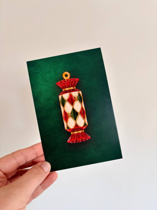 Hand holding a green Christmas greeting card with an embossed red, green, and gold jeweled Christmas cracker illustration.