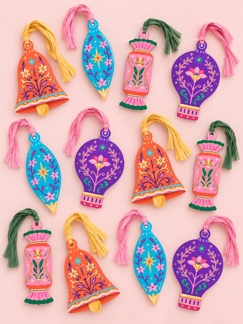 Twelve shaped paper ornaments in four Talisman folk-art floral designs — Bell, Finial, Candy, and Hot Air Balloon — in orange, blue, pink, and purple, each with a colorful raffia tassel, arranged on a pink background.